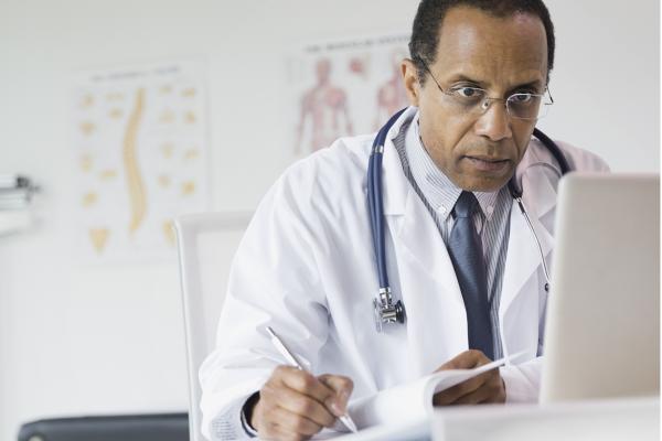 Physician taking notes from a computer screen.