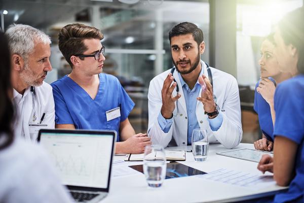 Six diverse physicians sit at a table and have a discussion.