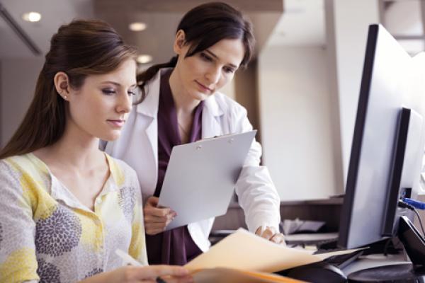 A physician looks over files with a member of her office staff.