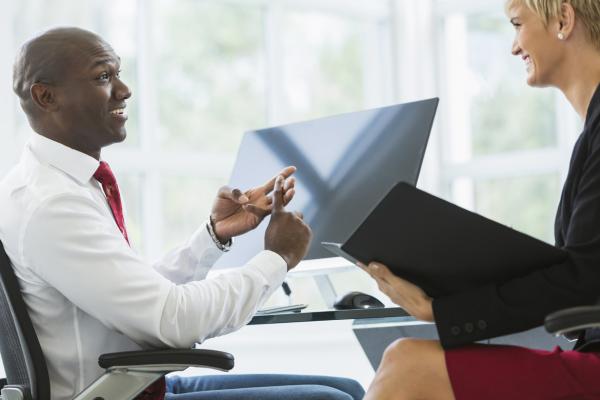 A photo of two people having a discussion at a computer in an office.