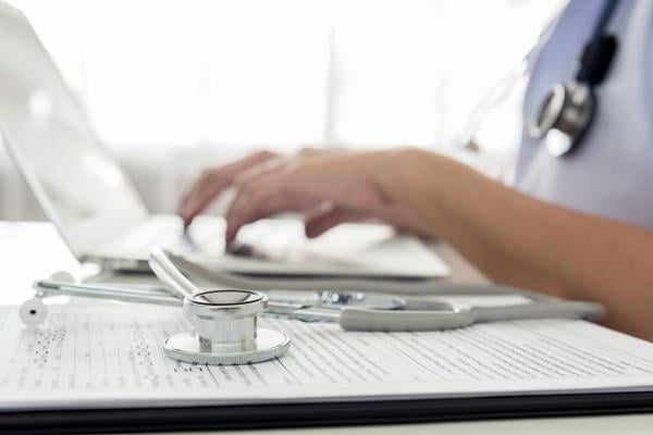 Close up photo of a physician using a laptop with her stethoscope to the side.